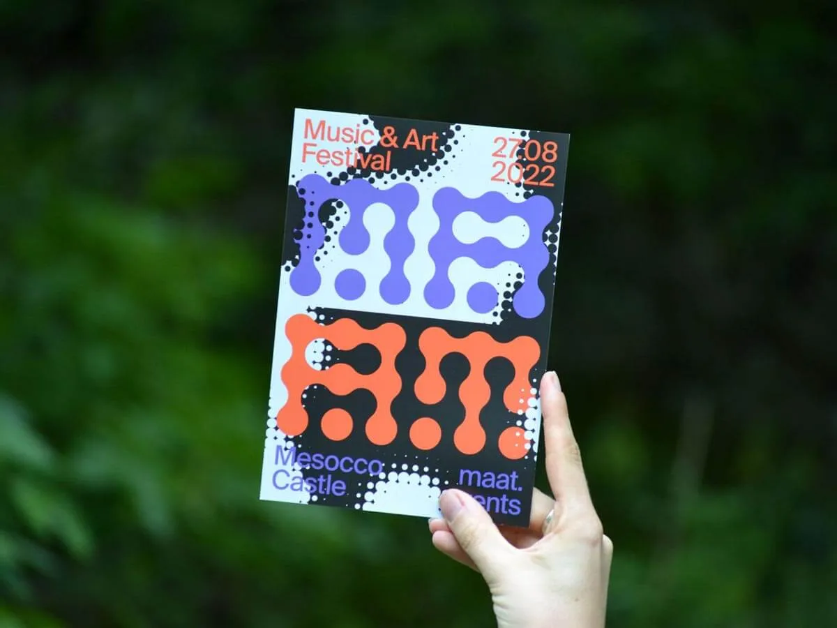 Hand holding a poster with abstract bubble-like text advertising a Music & Art Festival on 27.08.2022 at Mesocco Castle.