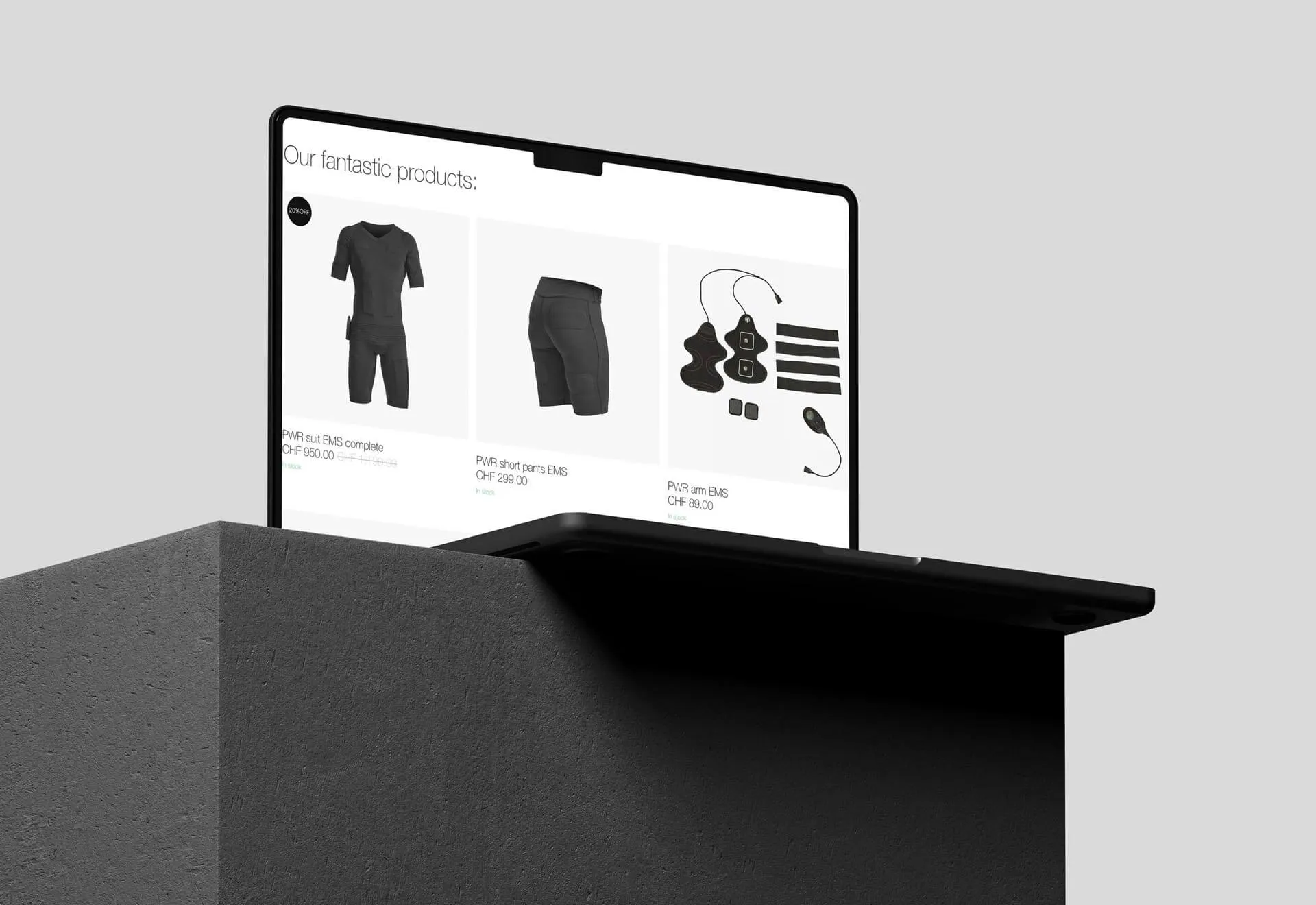 Laptop displaying a webpage with black EMS clothing products and accessories on a gray background.