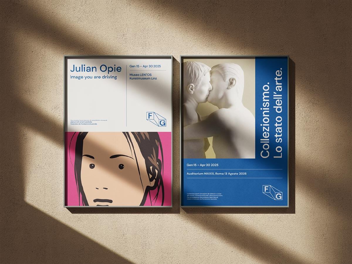 Two framed contemporary art posters on a textured wall with sunlight and shadows; one features a stylized face and the other shows a sculpture of two men kissing.