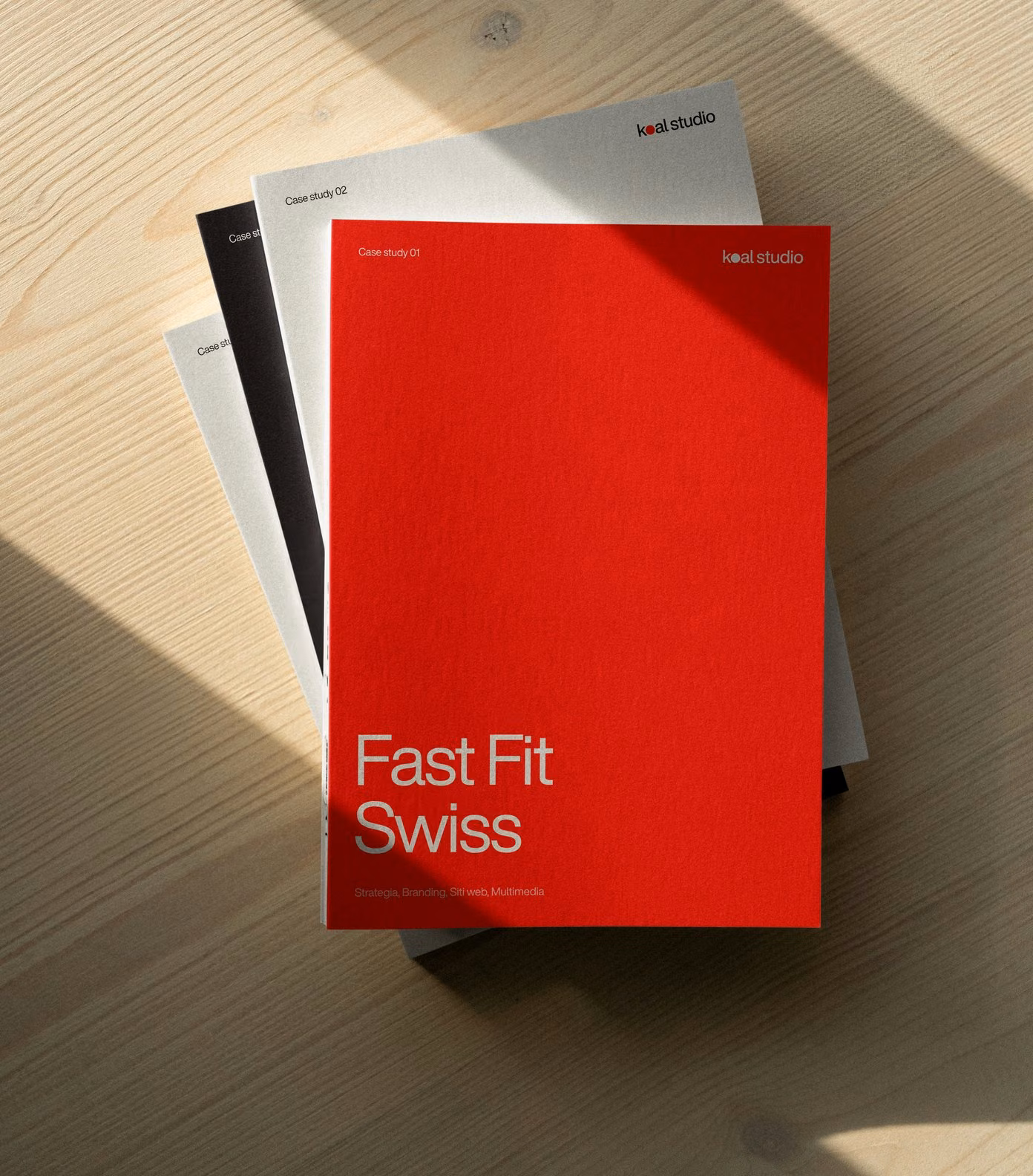 A stack of Koal Studio case study booklets, Fast Fit Swiss on top