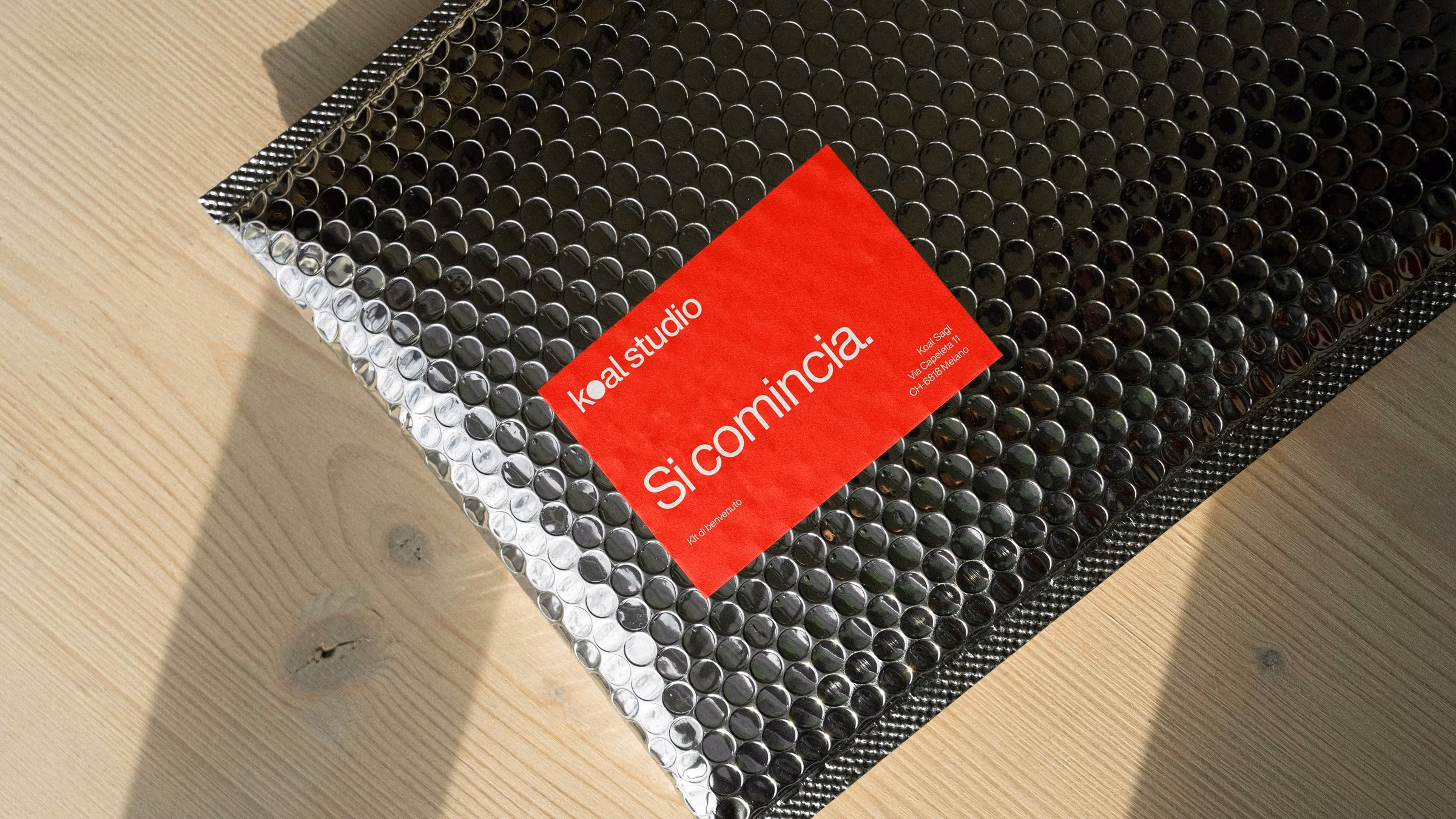 Black padded envelope with the red Koal Studio label: Si comincia, the welcome kit