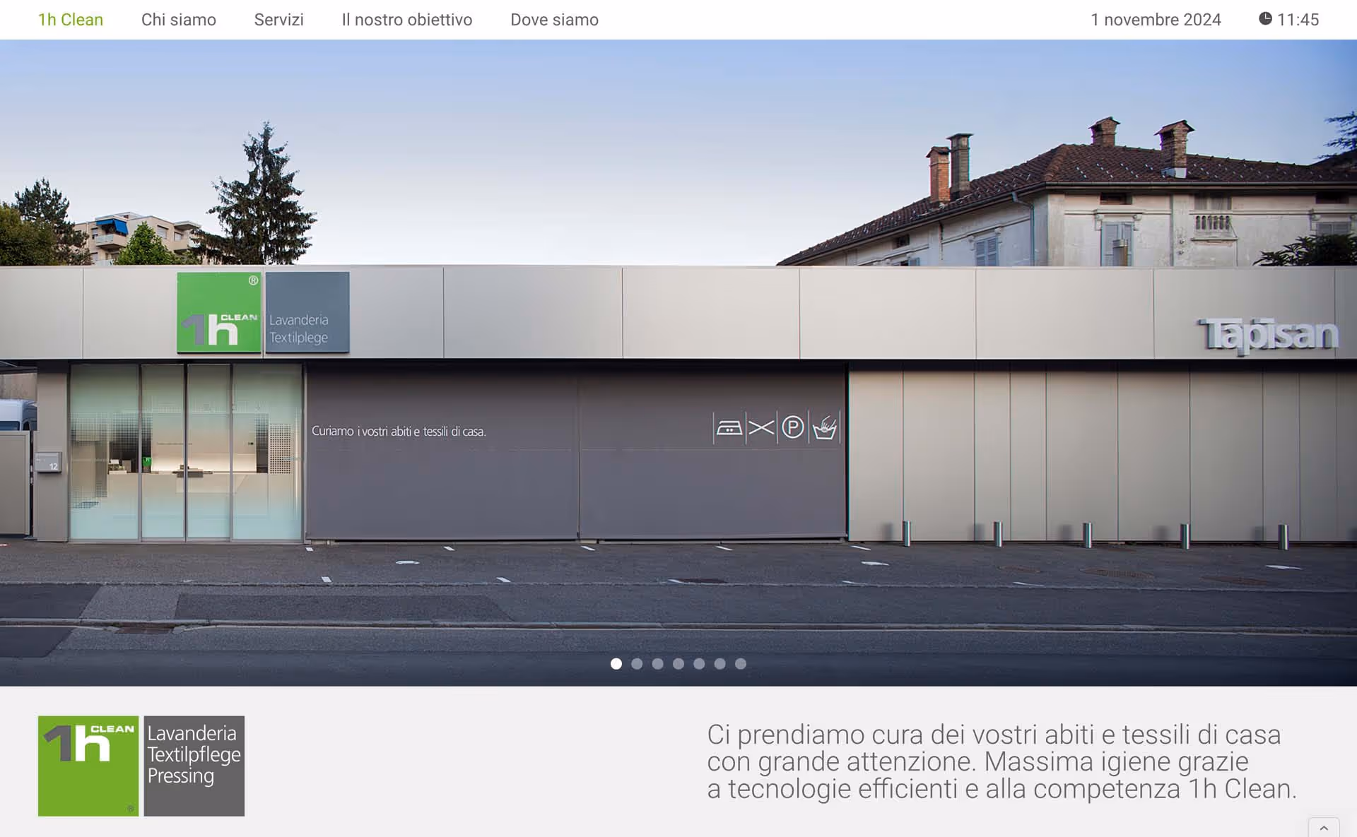 Exterior of 1h Clean laundry service building with a large garage door and adjacent glass entrance, signage includes '1h Clean Lavanderia Textilpflege' and 'Tapisan'.