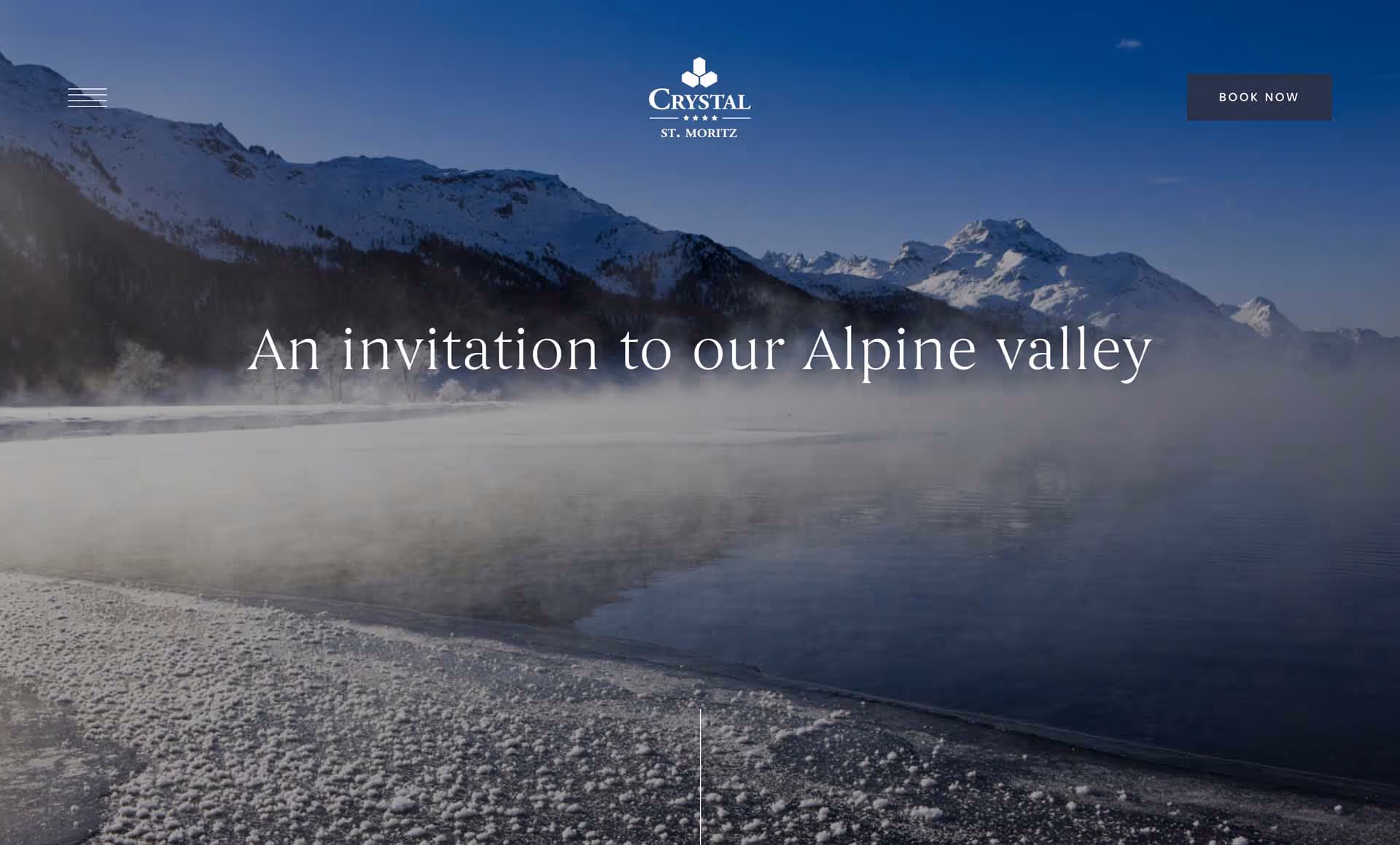 Snowy Alpine valley with mist rising over a calm dark lake and sunlit snow-covered mountains in the background.