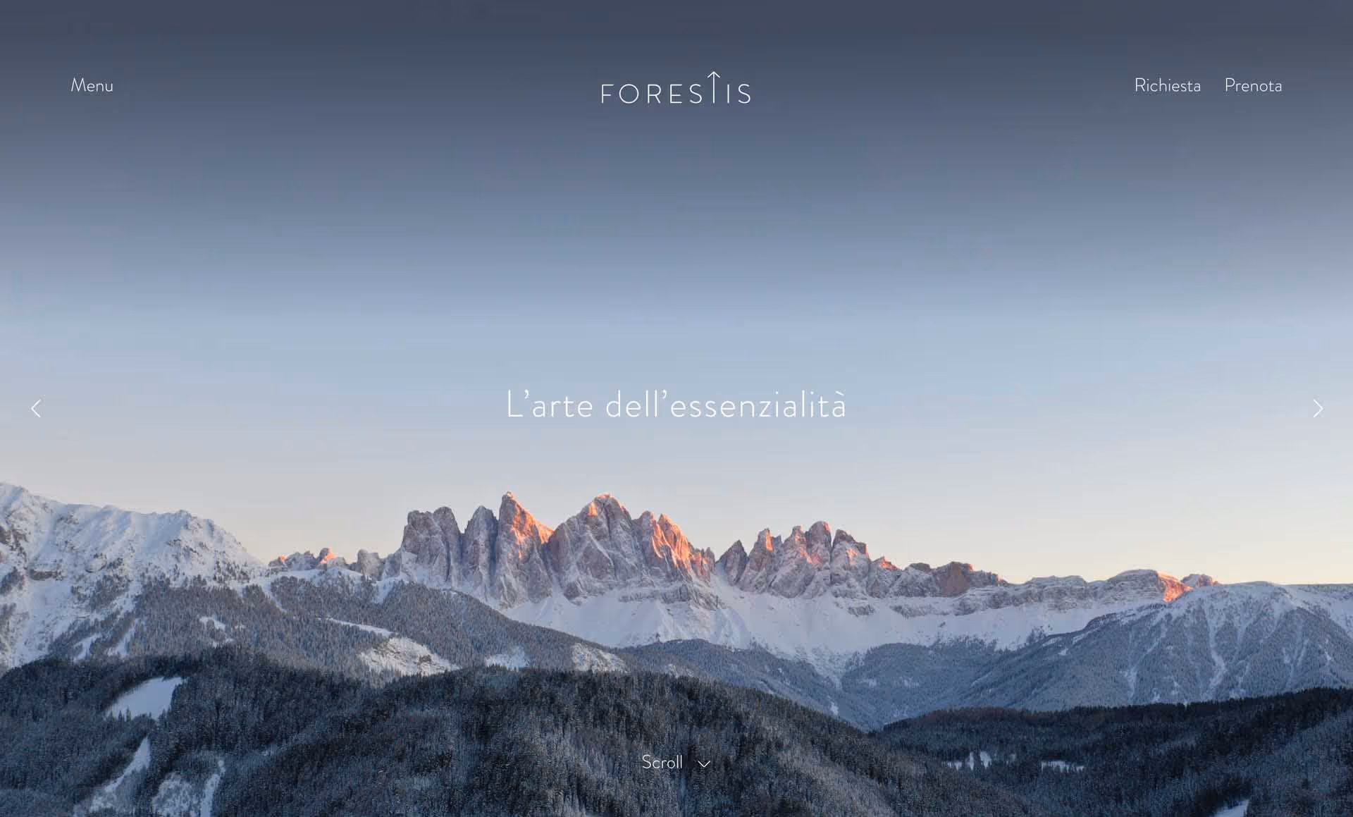 Snow-covered mountain peaks at sunrise with forested hills in the foreground and a clear sky.