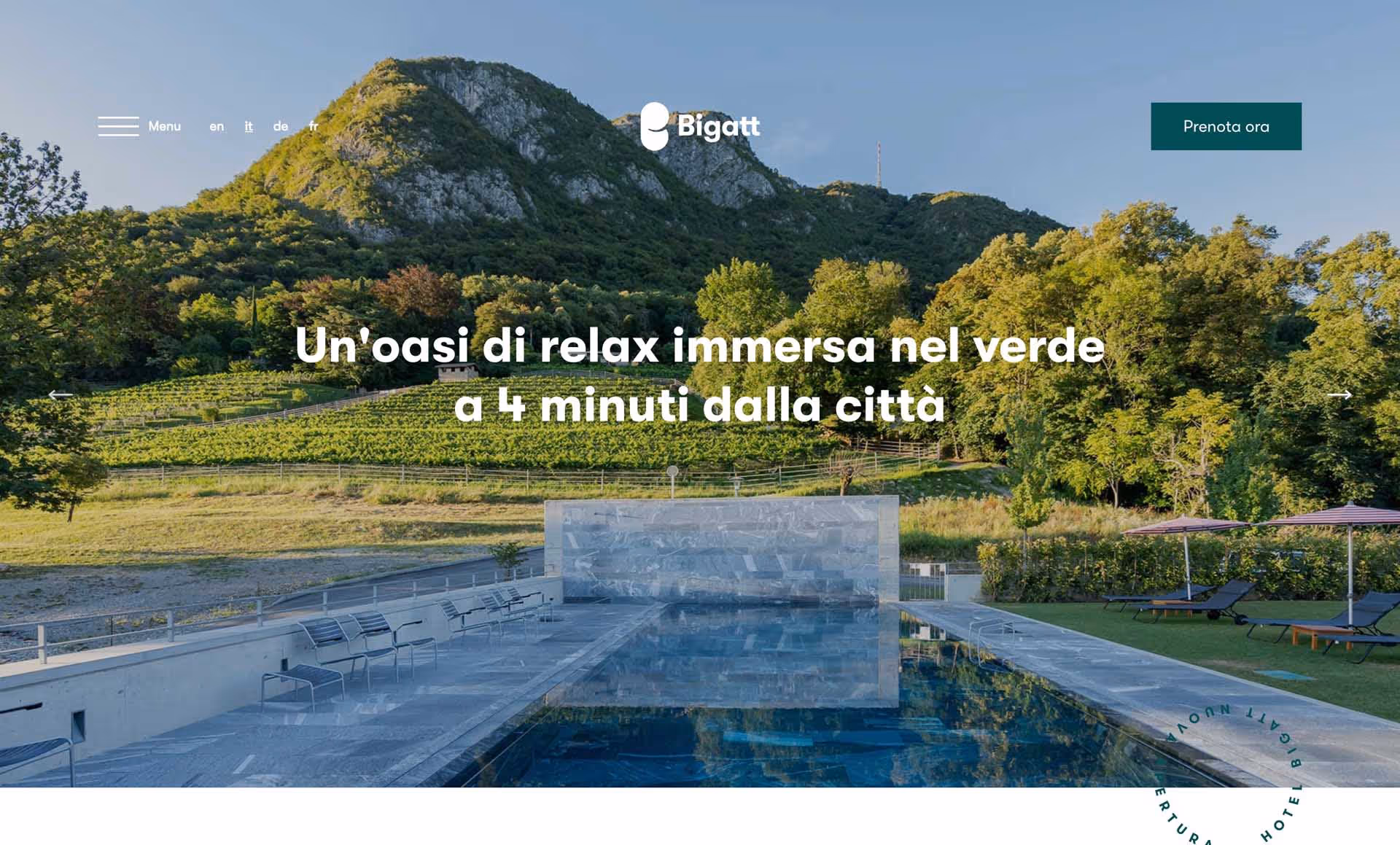Outdoor swimming pool with lounge chairs and umbrellas set against a backdrop of lush green hills and trees under a clear blue sky.