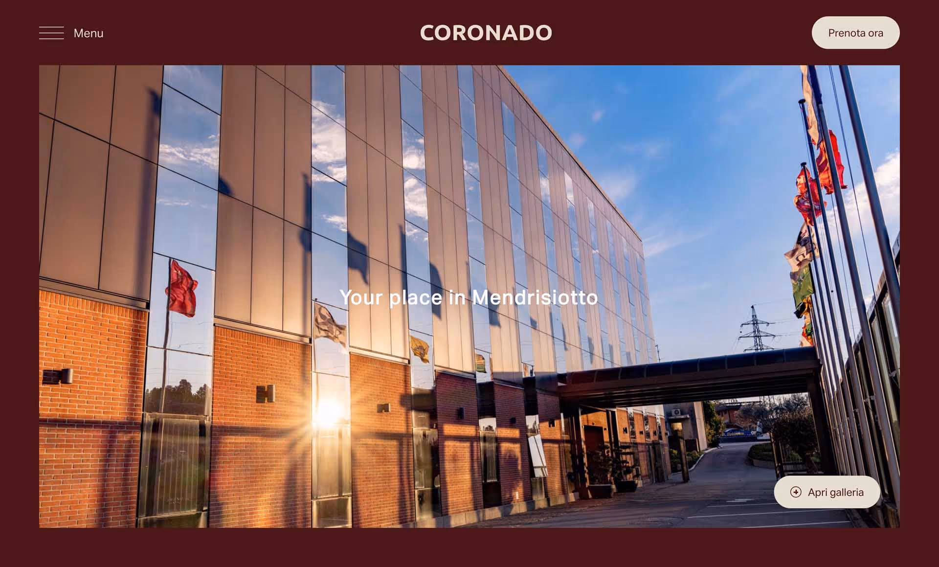 Modern building with reflective glass panels and brick walls, sun shining, and flags on poles beside the entrance.