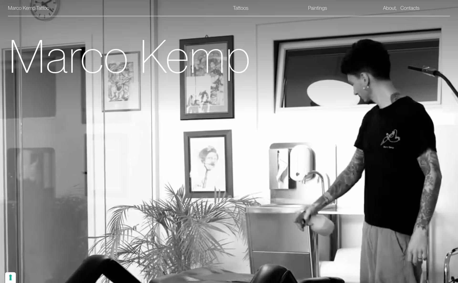 Tattoo artist in a studio spraying disinfectant on equipment with framed artwork and a plant in the background.