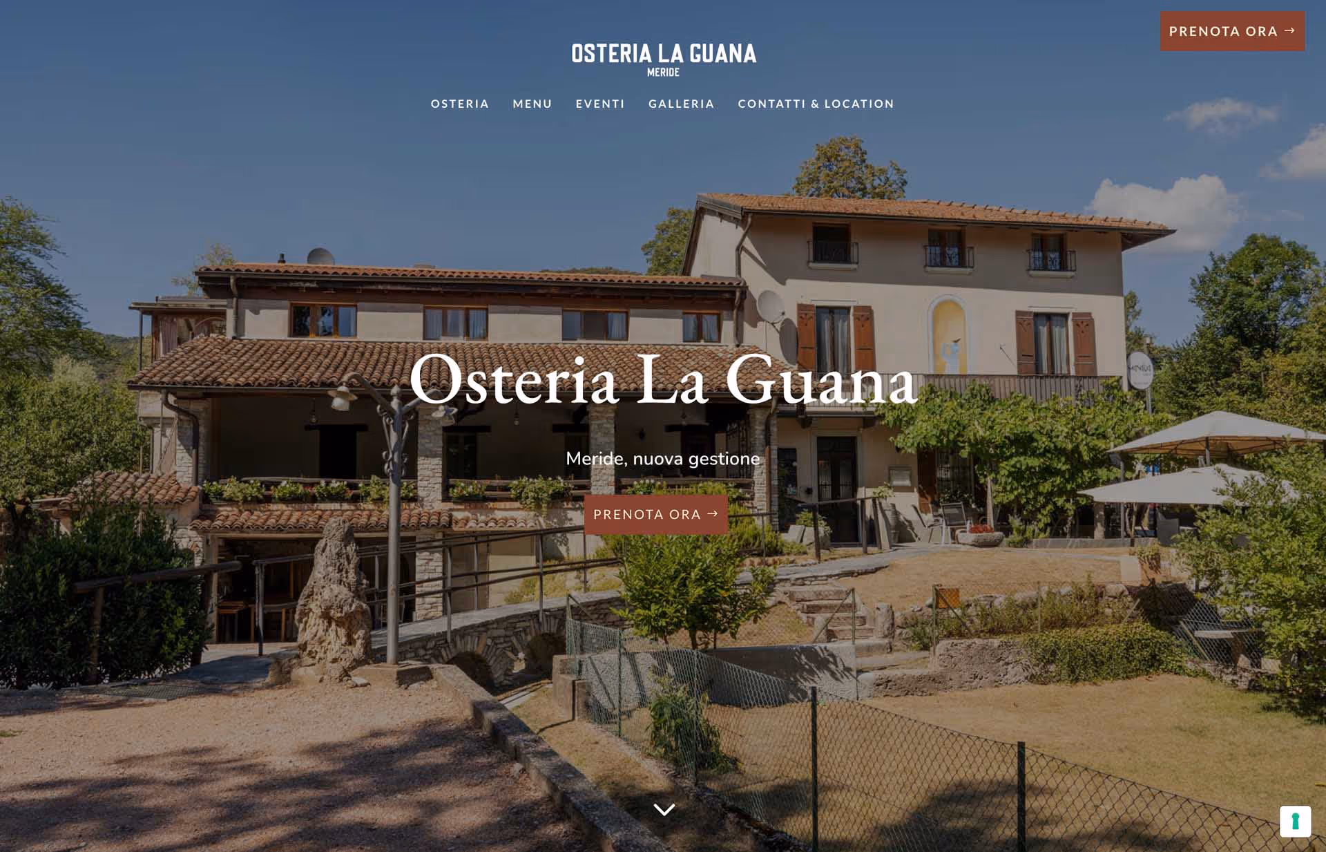 Exterior view of Osteria La Guana restaurant with a rustic building, greenery, and outdoor seating under umbrellas on a sunny day.