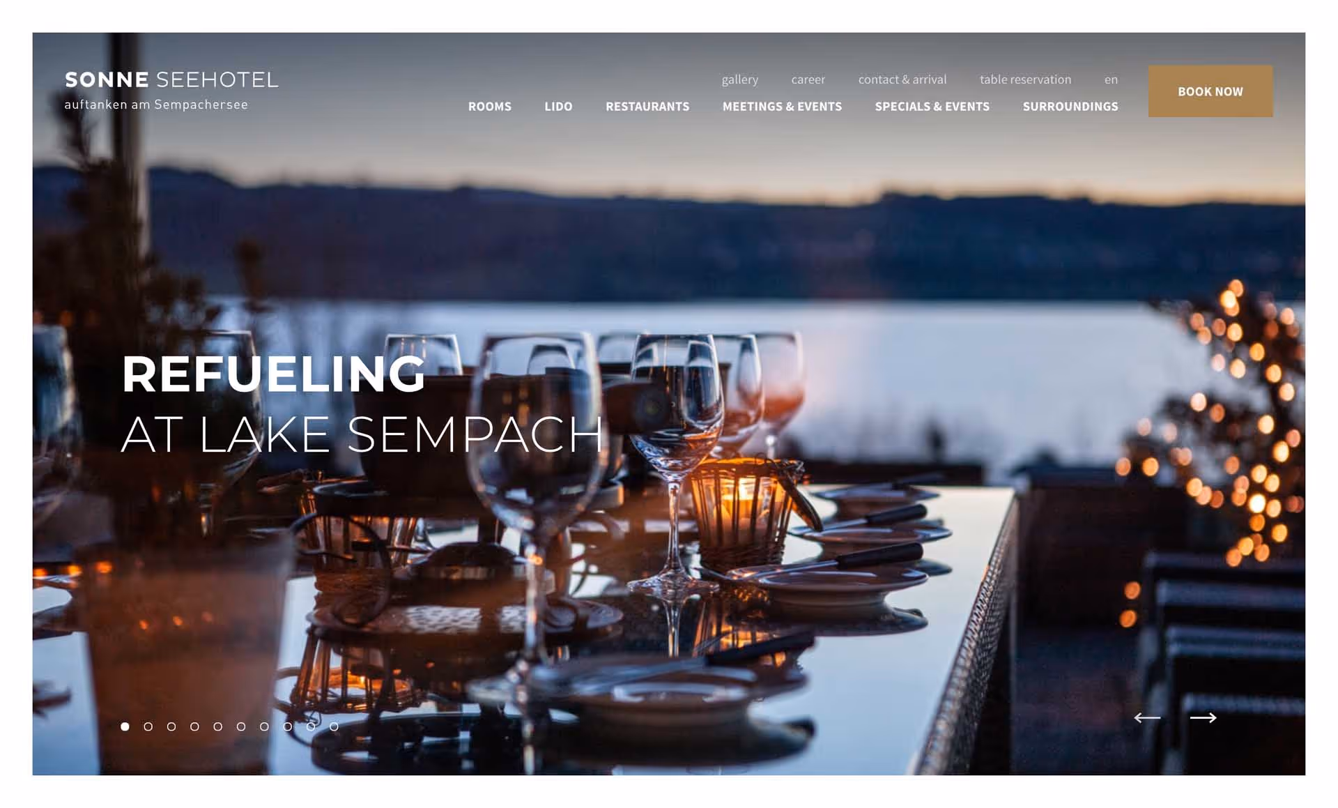 Elegant outdoor dining table set with wine glasses and plates overlooking a lake at dusk.