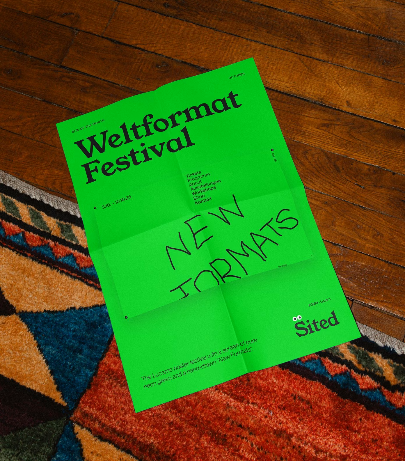 Site of the month poster folded on a rug: Weltformat Festival on neon green