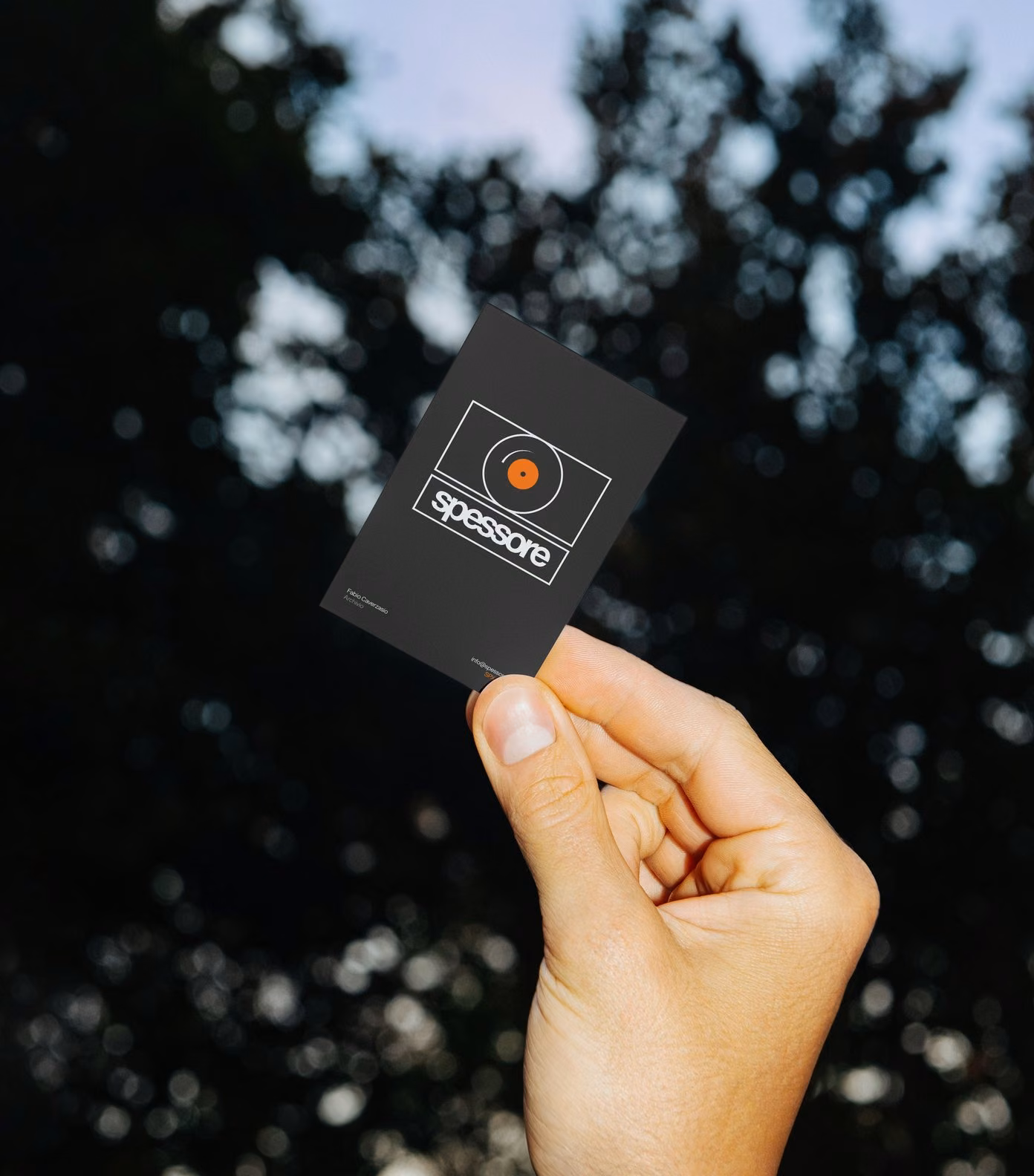 The black Spessore business card held up against the trees